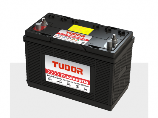 Black Tudor traction battery with red terminal cap and two posts on top, labeled Tudor Tractionária, resting on a light gray surface.